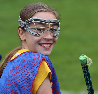 girl with lacrosse stick and mask smiling