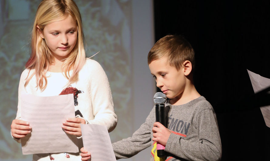 boy and girl reading a piece of paper on stage with a microphone