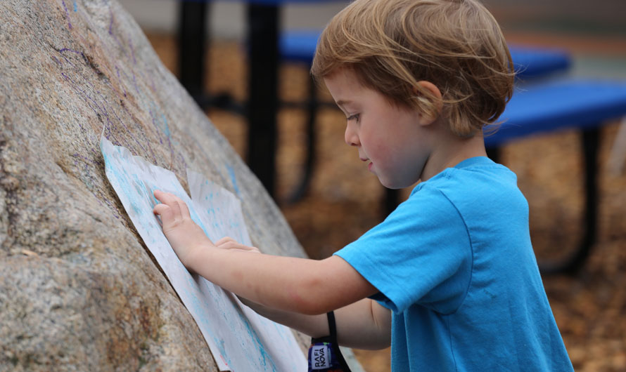 boy holding pictures against a rock