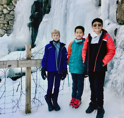 Three boys standing in front of frozen waterfall